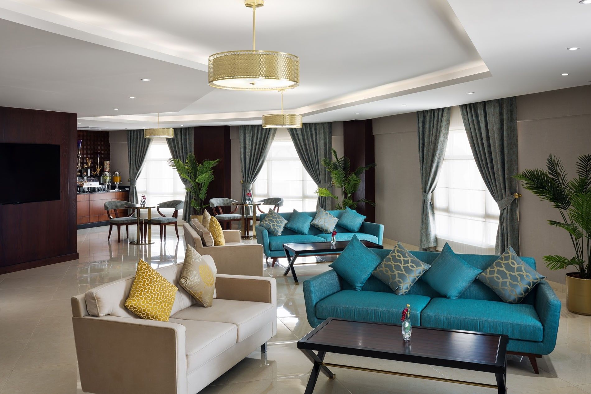 Lobby lounge featuring blue and beige sofas & gold lamps with small dining area at Saja Warwick Madinah