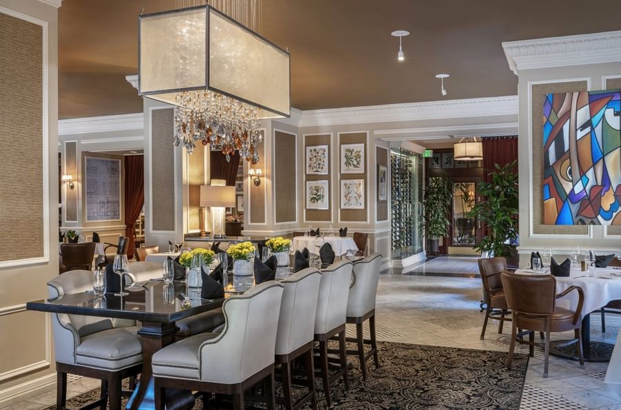 Dining tables with beige chairs under a crystal chandelier in The Landmark restaurant at Warwick Melrose Dallas