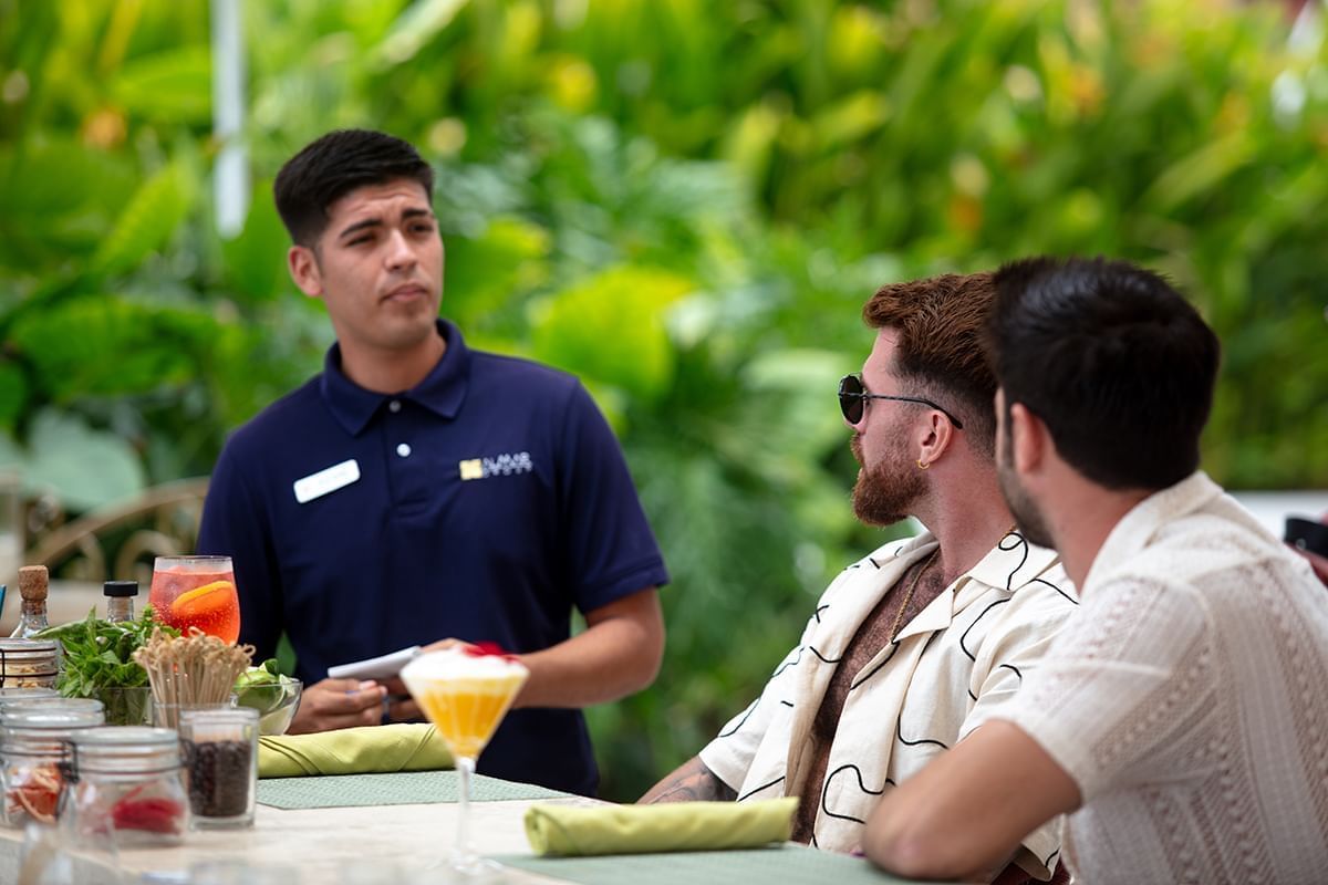 A waiter serving drinks to guests in the lush outdoor Red Fish Seafood restaurant at Almar Beach Resort