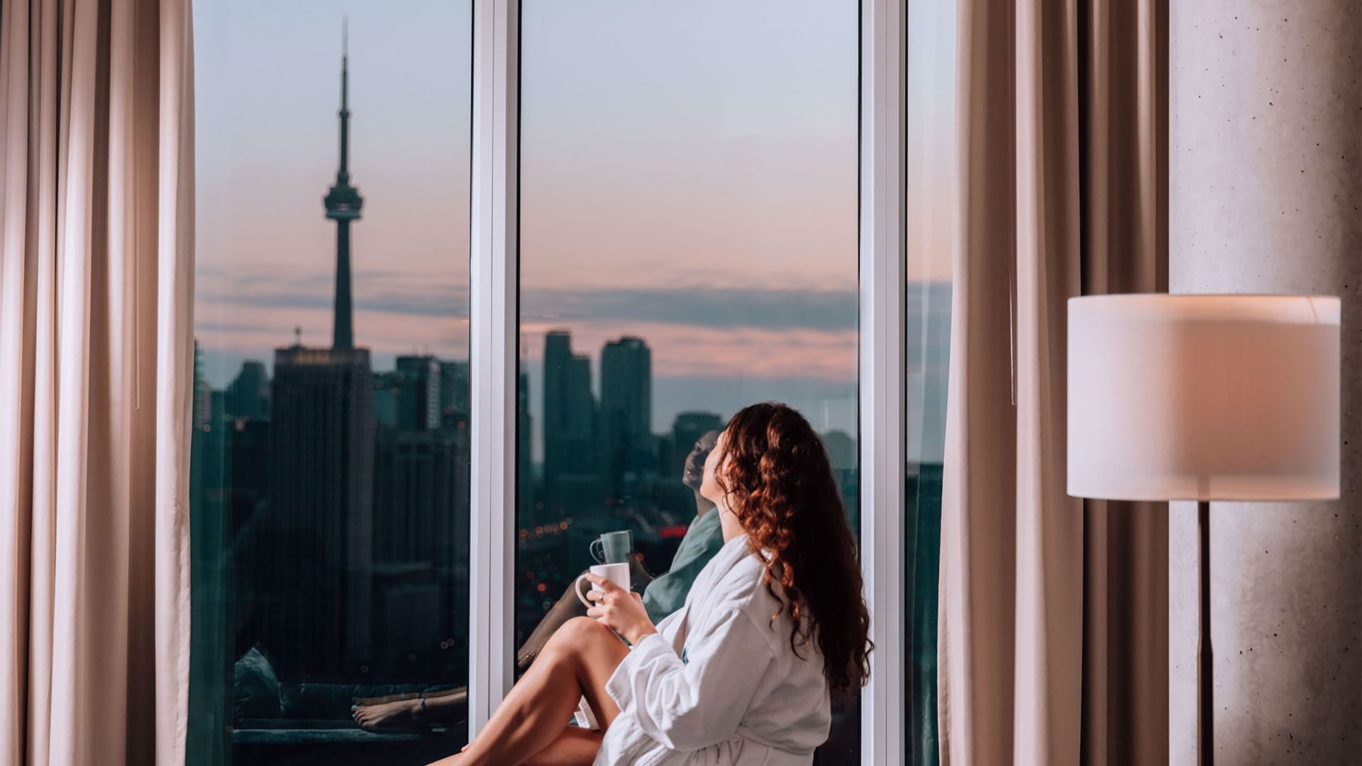 Femme tenant une tasse, regardant un paysage urbain à travers les fenêtres de l'hôtel X Toronto