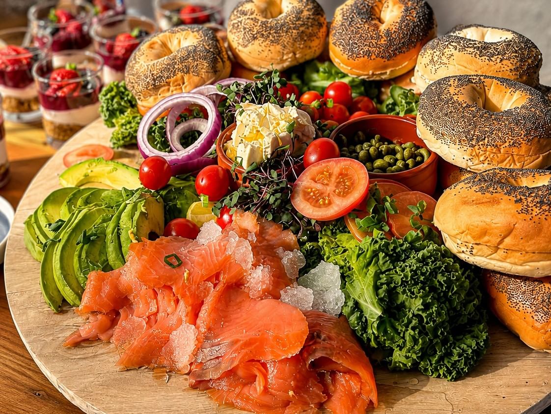 Breakfast platter featuring smoked salmon, bagels, avocado and fresh salad ingredients.