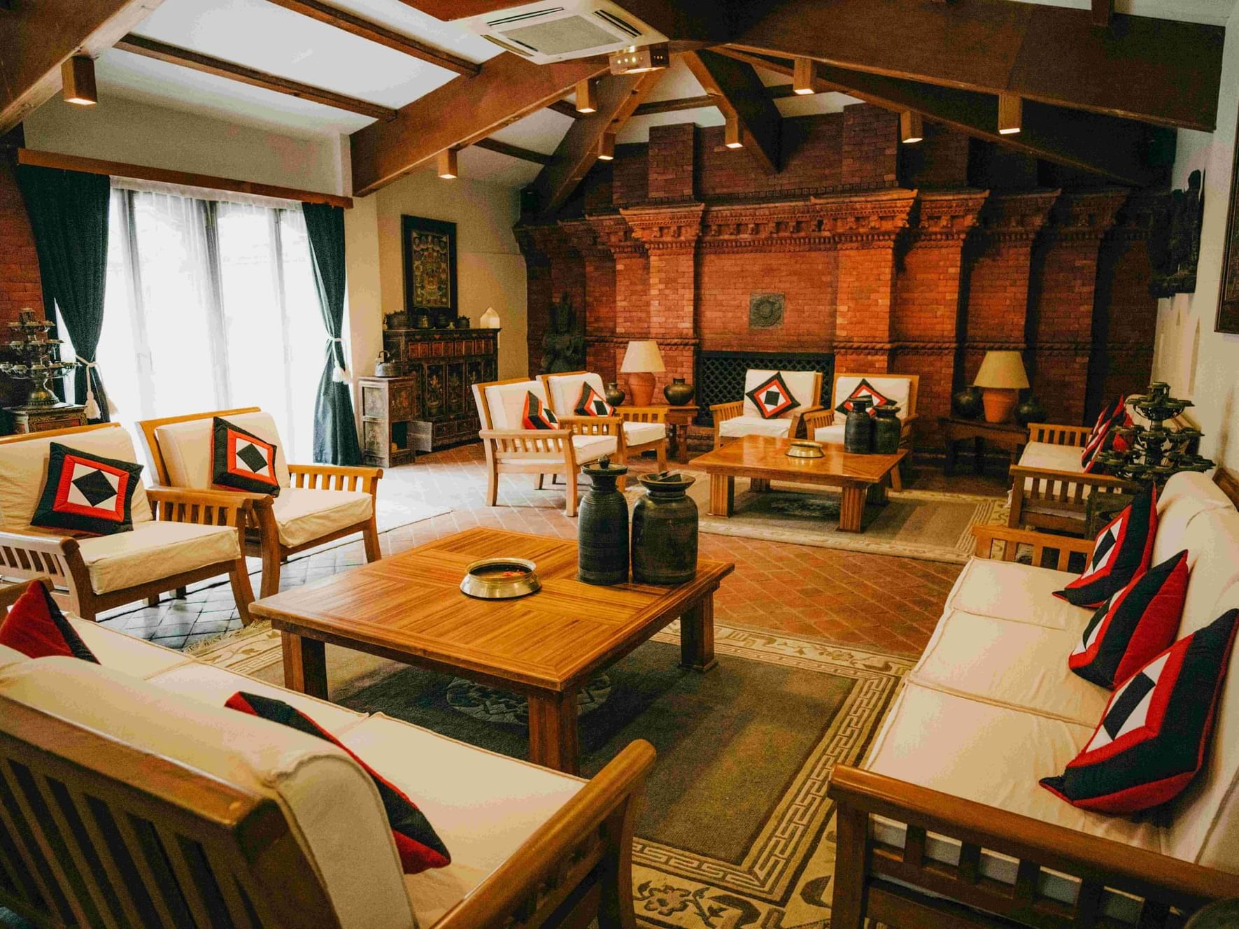Cozy Tara Lounge featuring wooden furniture, patterned cushions, and a warm brick wall with art at Dwarika's Hotel Kathmandu