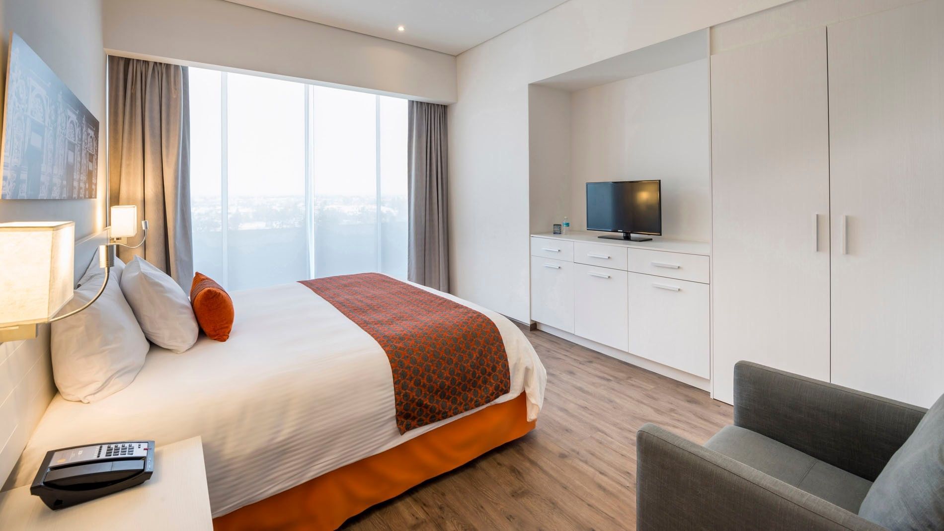Spacious King Standard room showing a white dresser with a TV and a cozy grey lounge chair at Camino Real Puebla Angelopolis