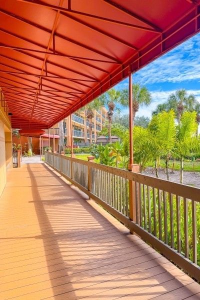 A covered walkway with a red awning beside a small lake with lots of greenery and palm trees at Rosen Inn Lake Buena Vista.