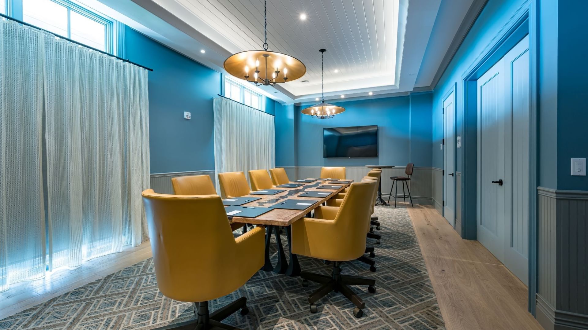 Boardroom with blue walls, yellow chairs around a wooden table, and pendant lighting at Camp Creek Inn in Inlet Beach.