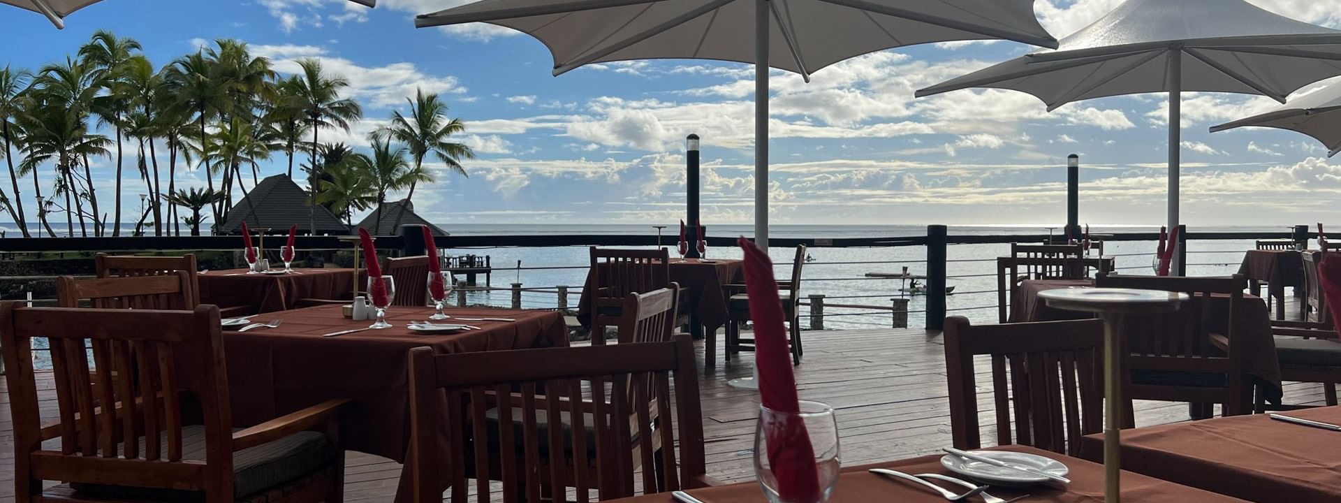 Wooden tables with red napkins by white umbrellas under a cloudy sky near the ocean at Warwick Hotels & Resorts
