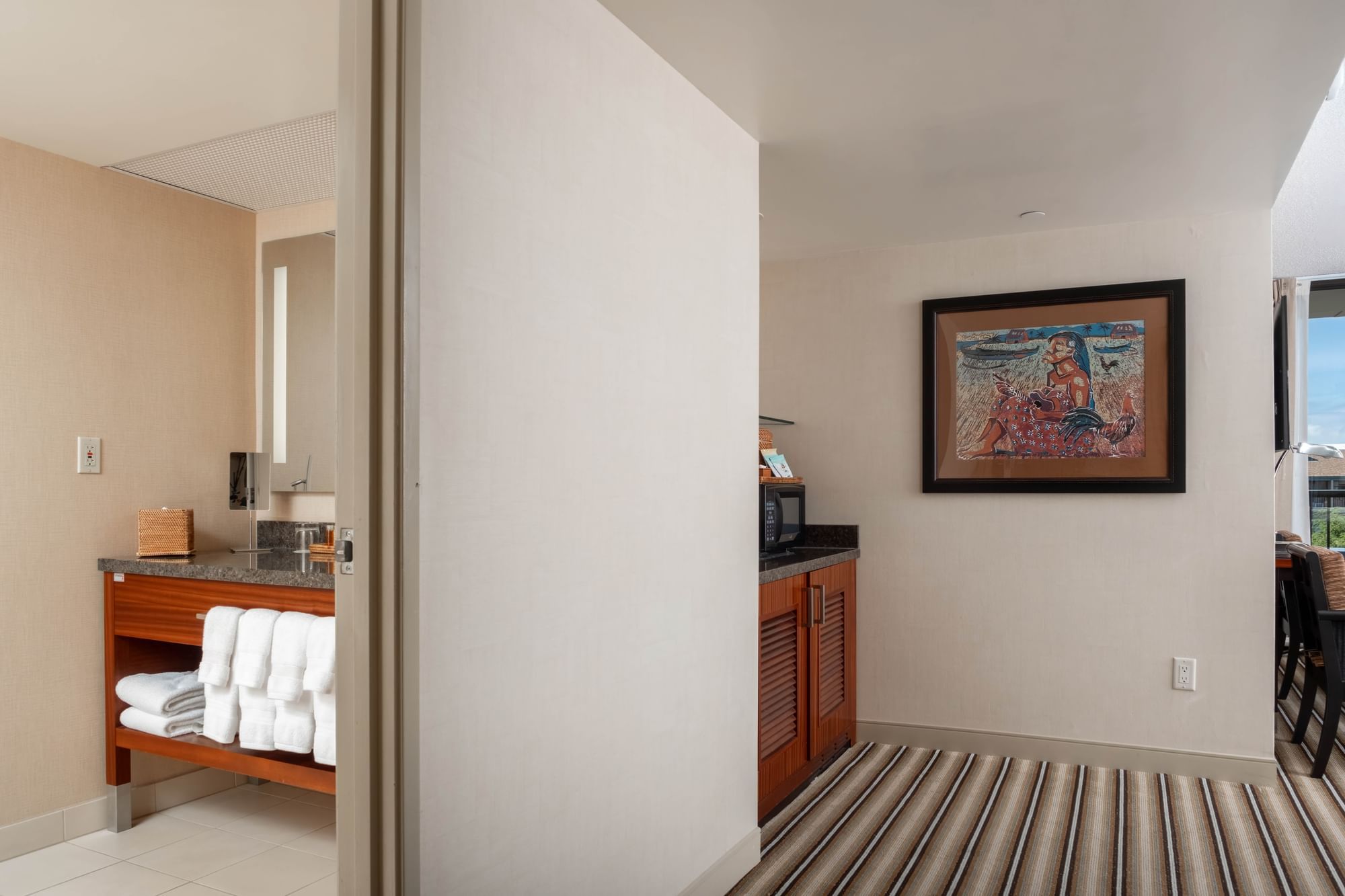 A hotel room with a coffee maker, towels, and artwork.