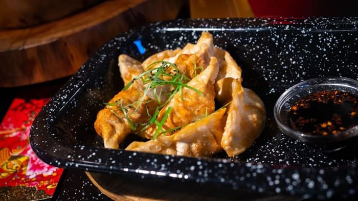 Pan-fried dumplings garnished with green onions next to dipping sauce in a tray at Media Sangre in Araiza Calafia