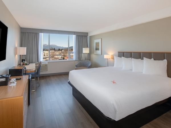 King-sized bed with a city view in a modern room at Coast Chilliwack Hotel by APA.