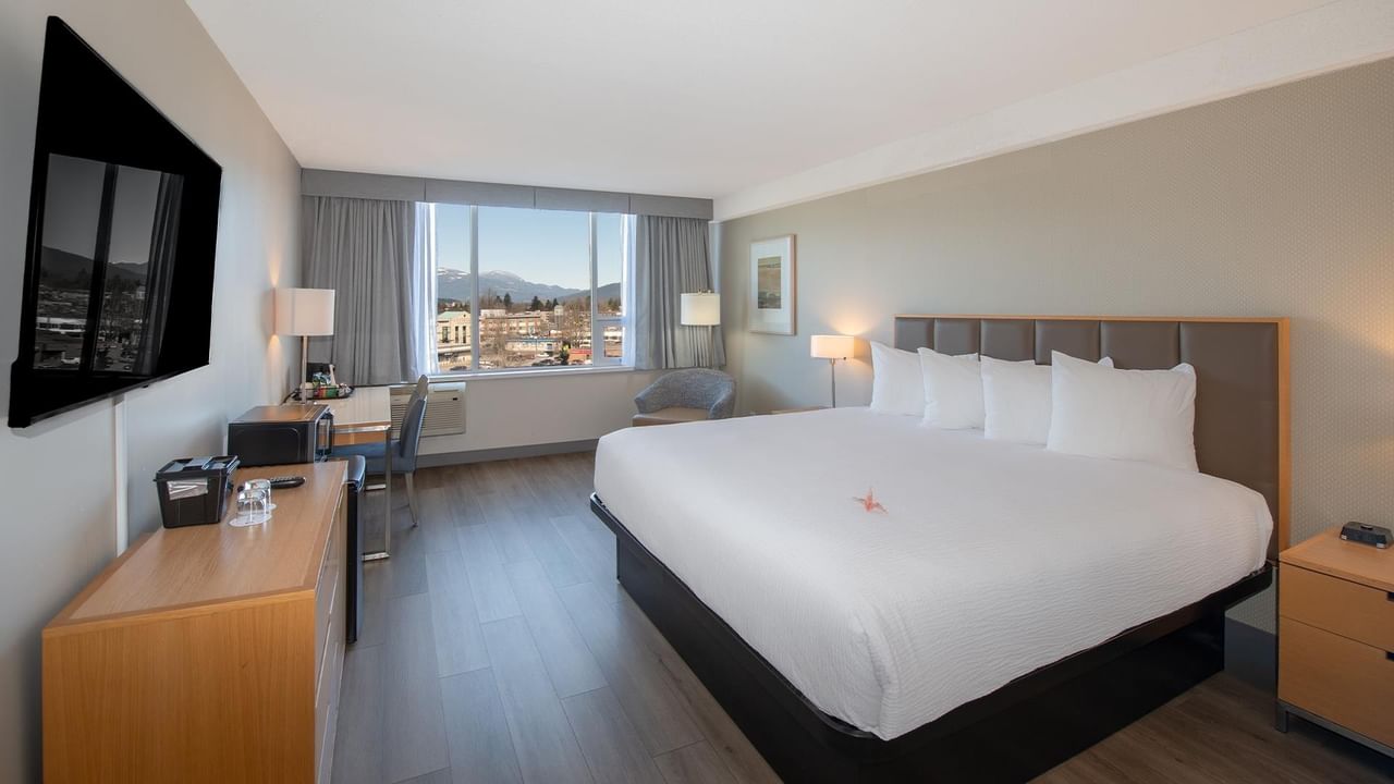 King-sized bed with a city view in a modern room at Coast Chilliwack Hotel by APA.