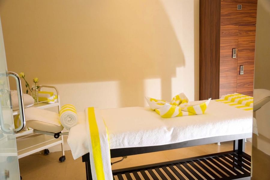 Spa treatment bed with yellow and white striped towels by a small cart at Warwick Al Khobar