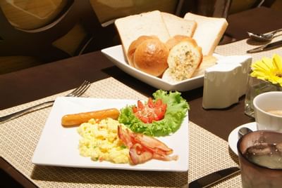 Breakfast served on a table with scrambled egg, bread and tea at Amora Neoluxe Hotel Bangkok