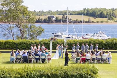 Outdoor wedding by a coastal marina with boats under a bright, sunny sky at Rodd Brudenell River Resort