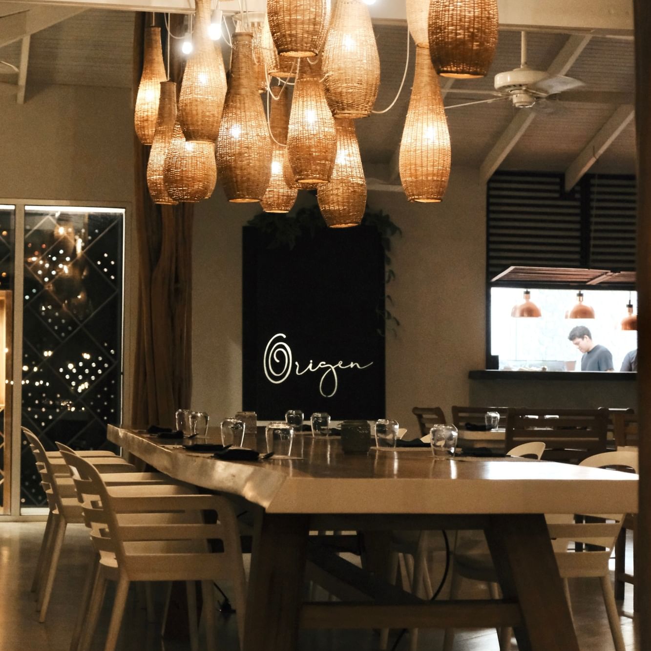 An elegant long dining table under woven pendant lights at the Origen restaurant at night at Cala Luna Boutique Hotel