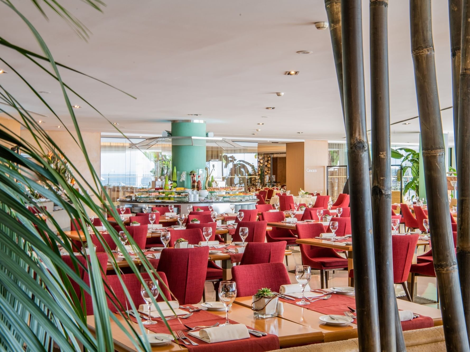 Restaurant luxueux avec chaises rouges, tables dressées, plantes exotiques et vue sur l'océan.