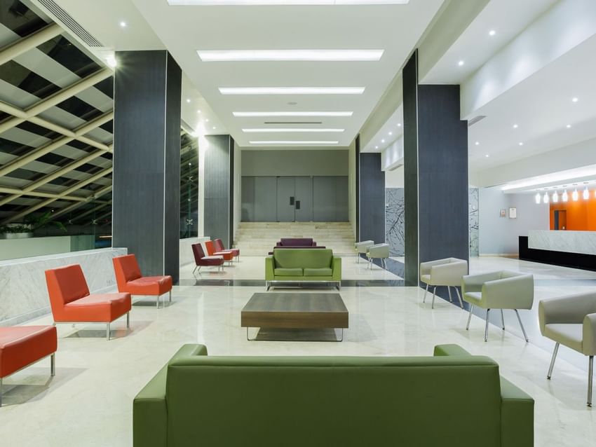 Modern lobby area with green and orange seating, high ceilings, and marble floors at Real Inn Tijuana