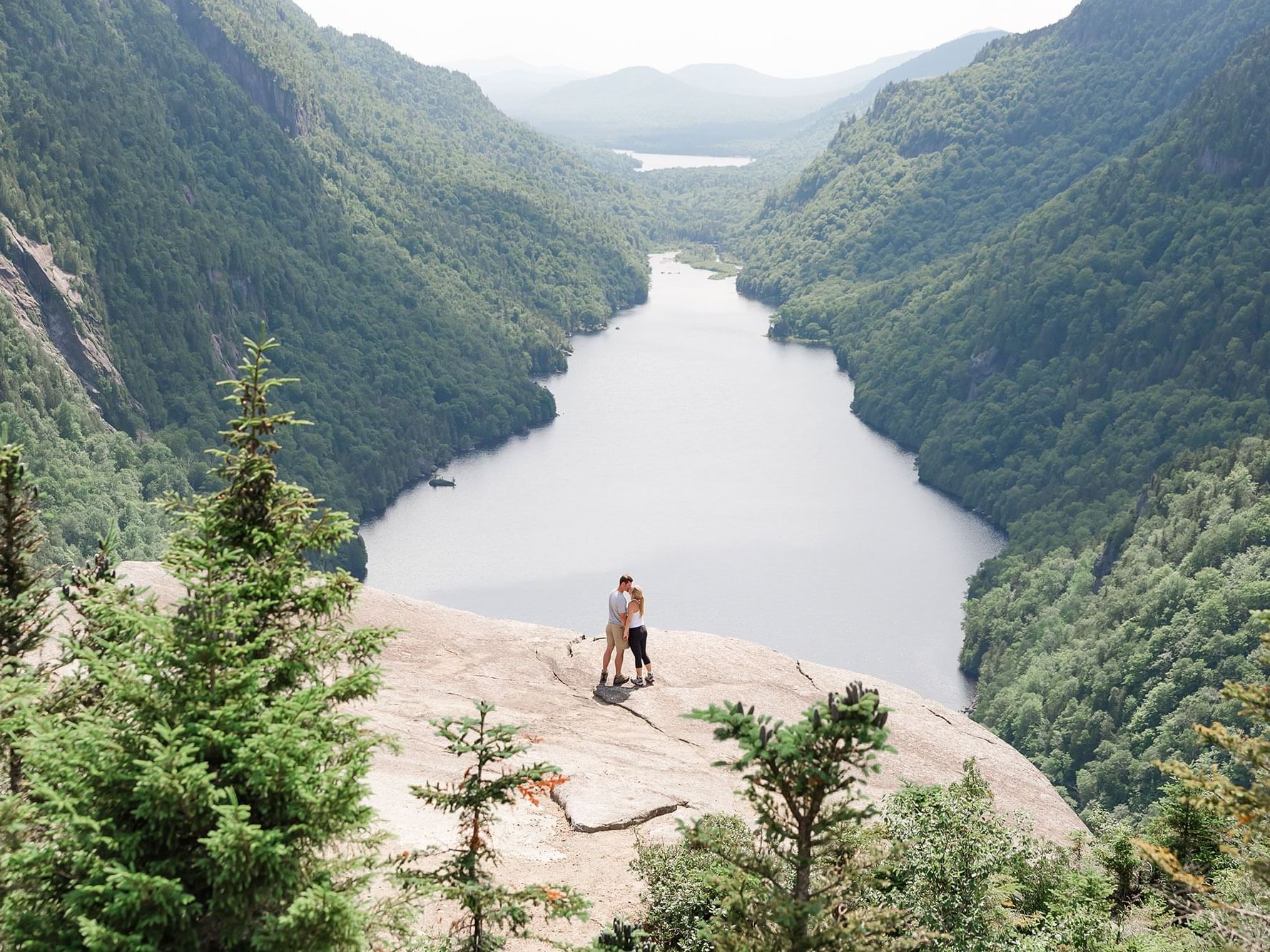 Couple standing on a rock overlooking a valley with a river and dense forest near High Peaks Resort