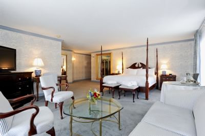Four-poster king bed and seating area with a glass table in the guest room at Farmington Inn and Suites