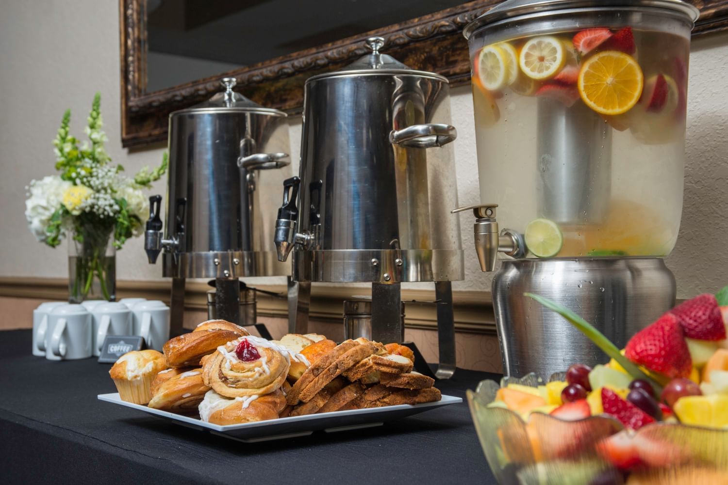 A breakfast buffet with pastries, fruit, and flavored beverages.
