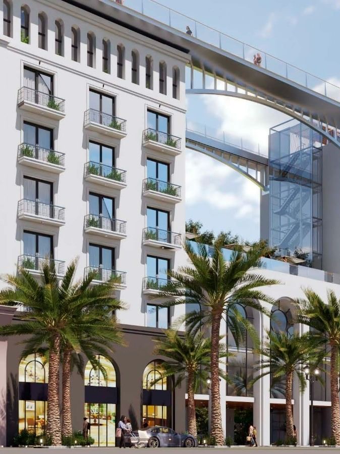 Façade moderne d'un hôtel de luxe avec palmiers et grandes baies vitrées cintrées sous un ciel bleu lumineux.