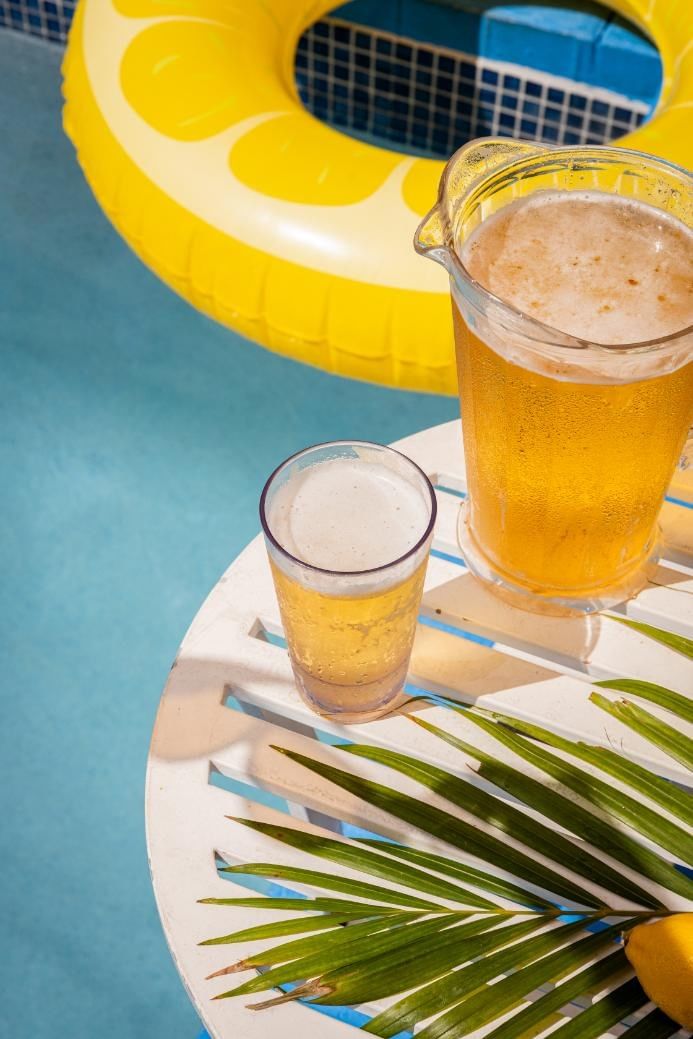 a pitcher and glass of beer on a table by the pool