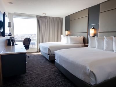Two beds with white bedding, a desk, and large window at Carriage House Hotel & Conference Centre