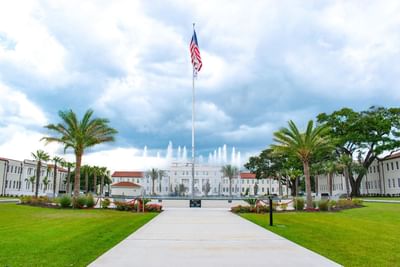 Grand lawn with a tall flagpole and dancing water fountain leading to the main building facade near Centennial Plaza Resort
