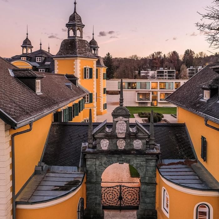 Elevated view of ornate hotel entrance with yellow buildings and a distant modern structure at Falkensteiner Schlosshotel Velden