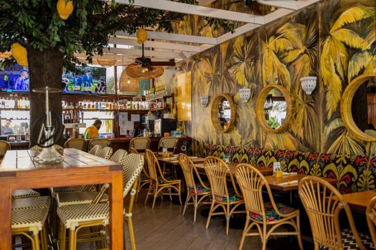 a dining area with a bar, tables, chairs, and tropical wallpaper