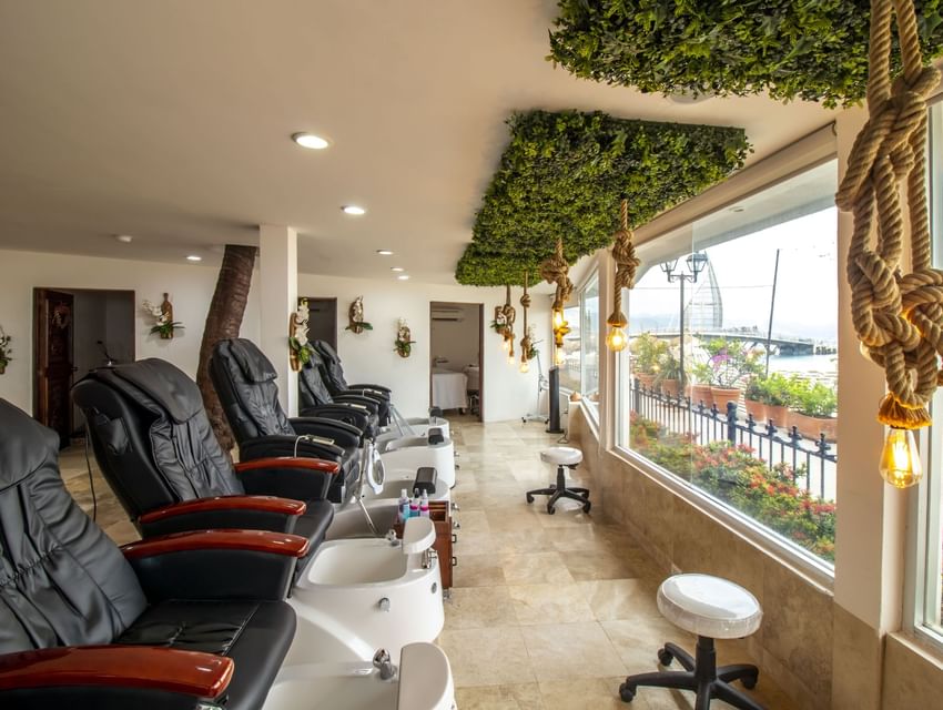 Spa pedicure area with black massage chairs, white foot basins, and tropical decor at Playa Los Arcos Puerto Vallarta 2023