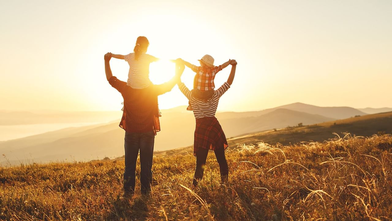 Family raising their arms toward the sunset, with children on their shoulders in a grassy field near Coast Penticton Hotel