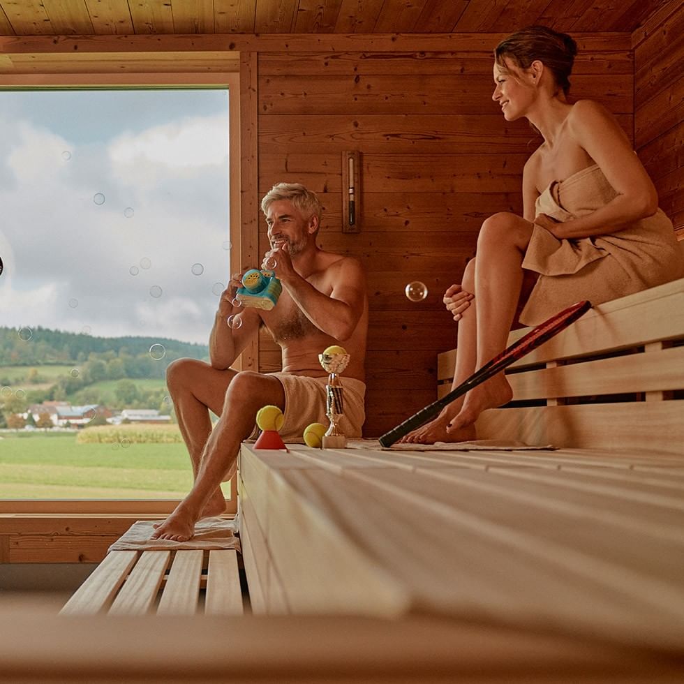 Zwei Personen genießen das Event Sauna: Infusion Weekend in einer hölzernen Sauna.