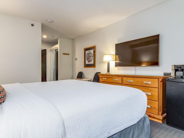A hotel room with a bed, dresser, TV, refrigerator, and coffee maker.