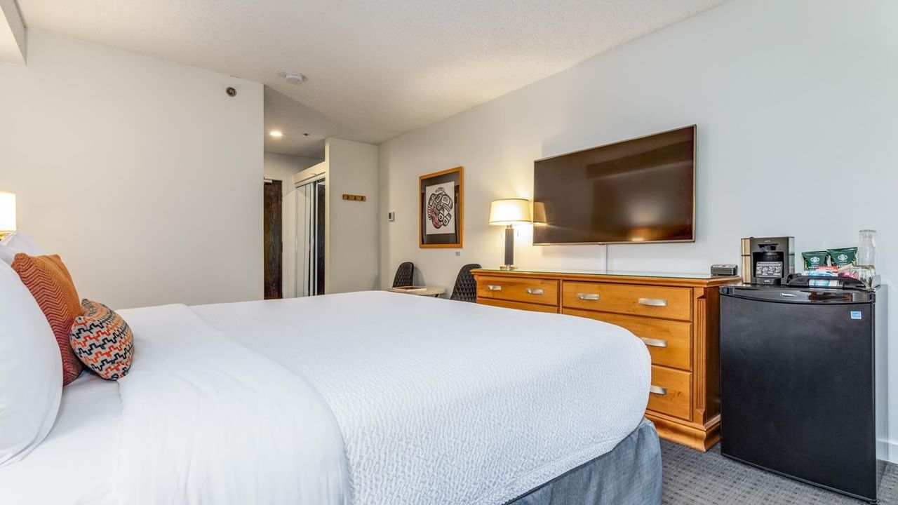 A hotel room with a bed, dresser, TV, refrigerator, and coffee maker.