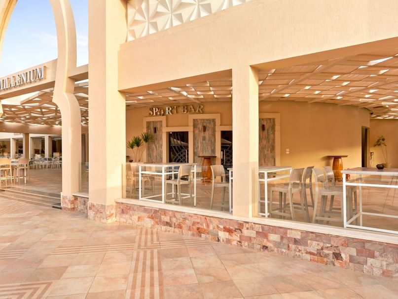 Outdoor seating area with white tables and chairs in front of a modern building labeled 