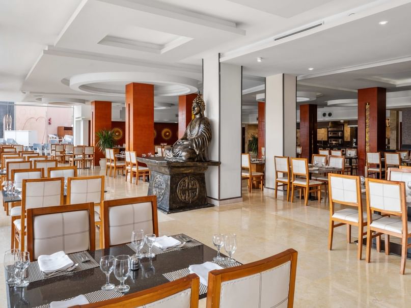 Elegantes Restaurant mit vielen Tischen, Stühlen, einer Buddha-Statue und moderner Inneneinrichtung.