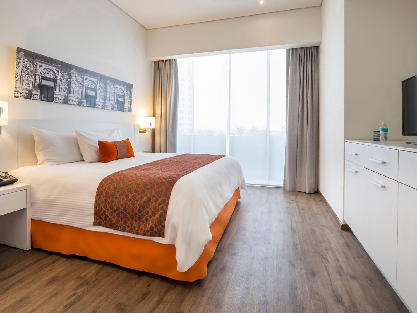 Queen Standard room featuring a bed with orange accents and large bright windows at Camino Real Puebla Angelopolis