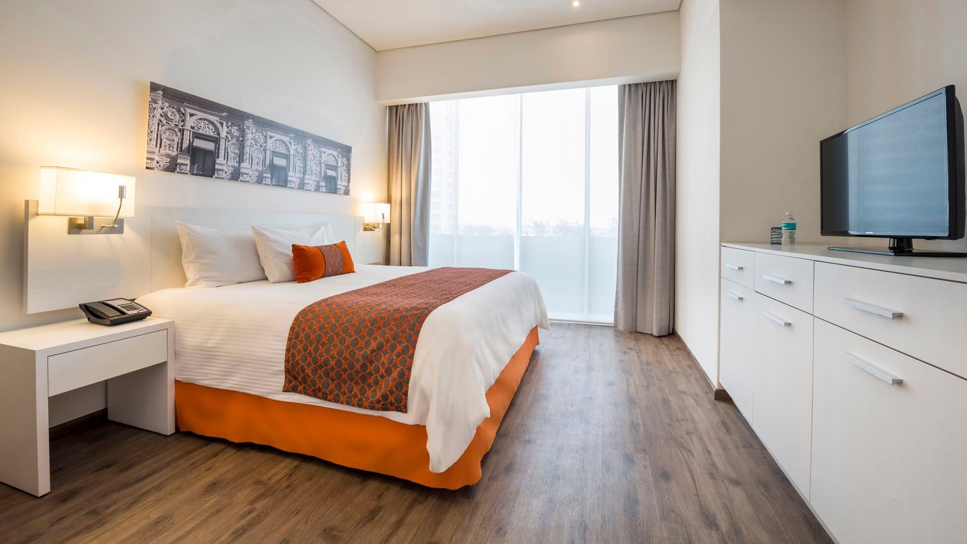 Queen Standard room featuring a bed with orange accents and large bright windows at Camino Real Puebla Angelopolis