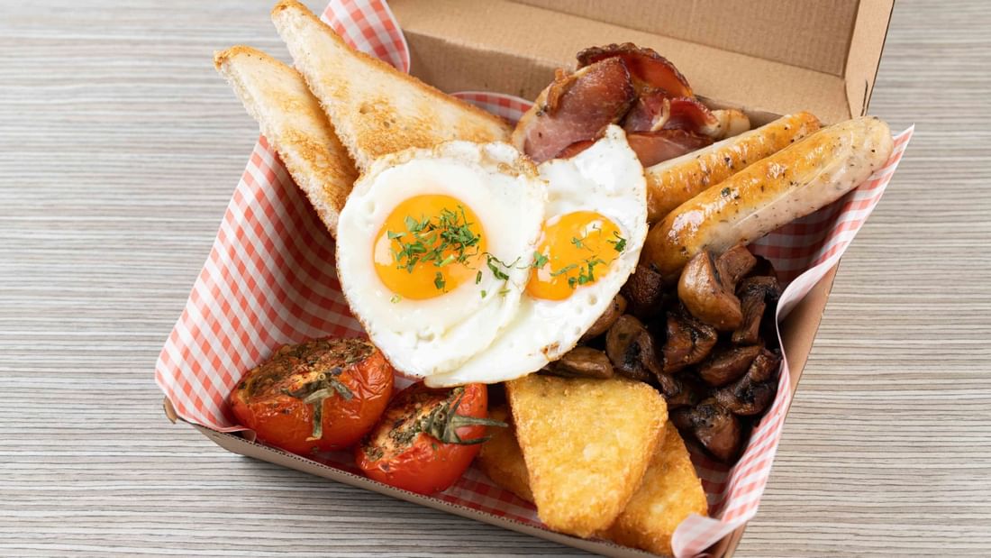 Full English breakfast in a takeaway box, featuring eggs, bacon, sausages, and toast served in Grab & Go at Ibis Adelaide