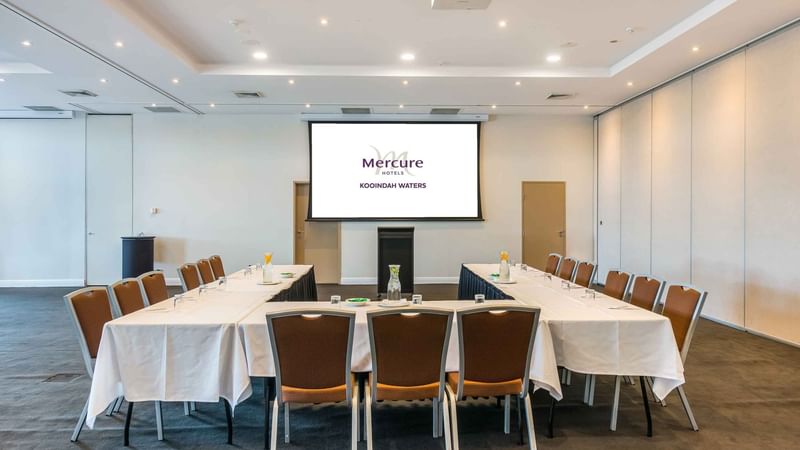 Kooindah Two Meeting room set up with tables, chairs, and a presentation screen at Mercure Kooindah Waters