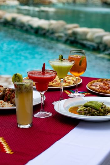 Colorful cocktails and gourmet dishes on a red runner by a stone-lined pool at Hotel Chan-kah Resort Village