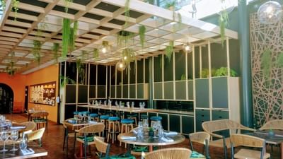 Intérieur d'un restaurant avec tables, chaises, plantes suspendues, et un plafond en bois.