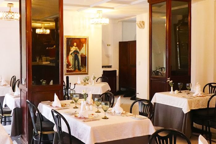 Elegant dining room with white-clothed tables, dark wood chairs, and classic portrait at Playa Los Arcos Puerto Vallarta 2023