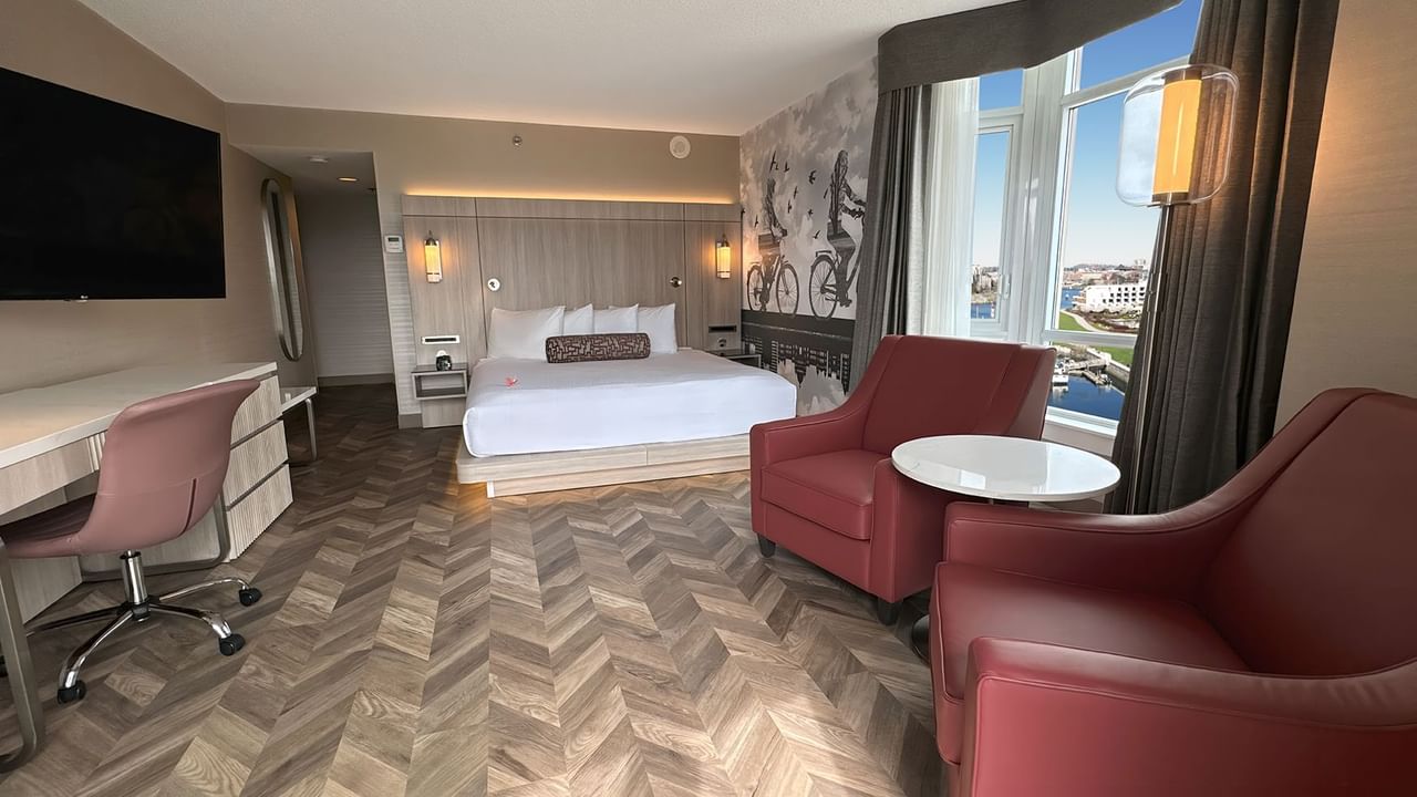 Hotel guestroom with bed, window, TV, work desk, and two sofas.