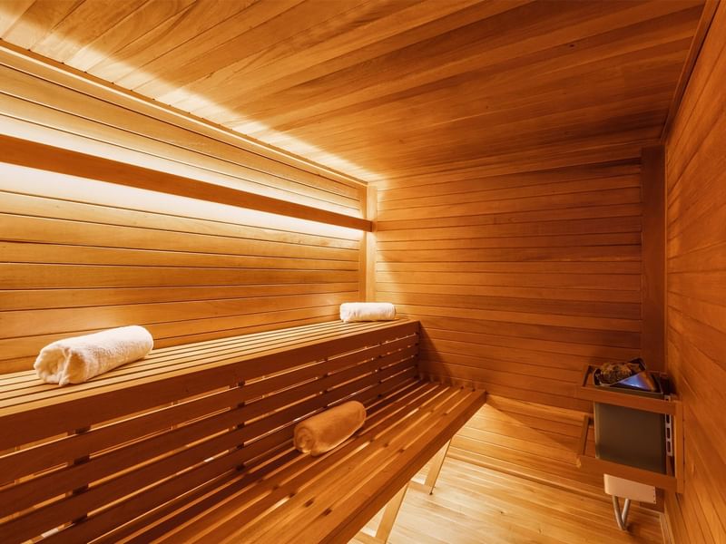 Serene wooden sauna with two tiers of benches and soft lighting, located at Fiesta Americana for guest relaxation