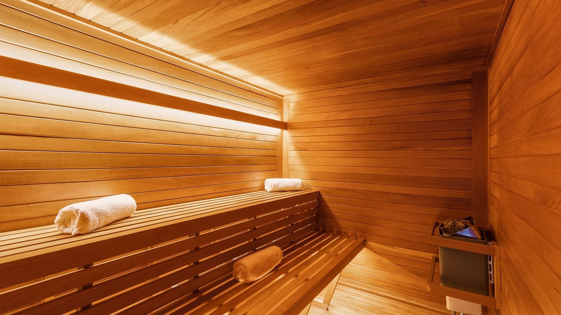 Serene wooden sauna with two tiers of benches and soft lighting, located at Fiesta Americana for guest relaxation