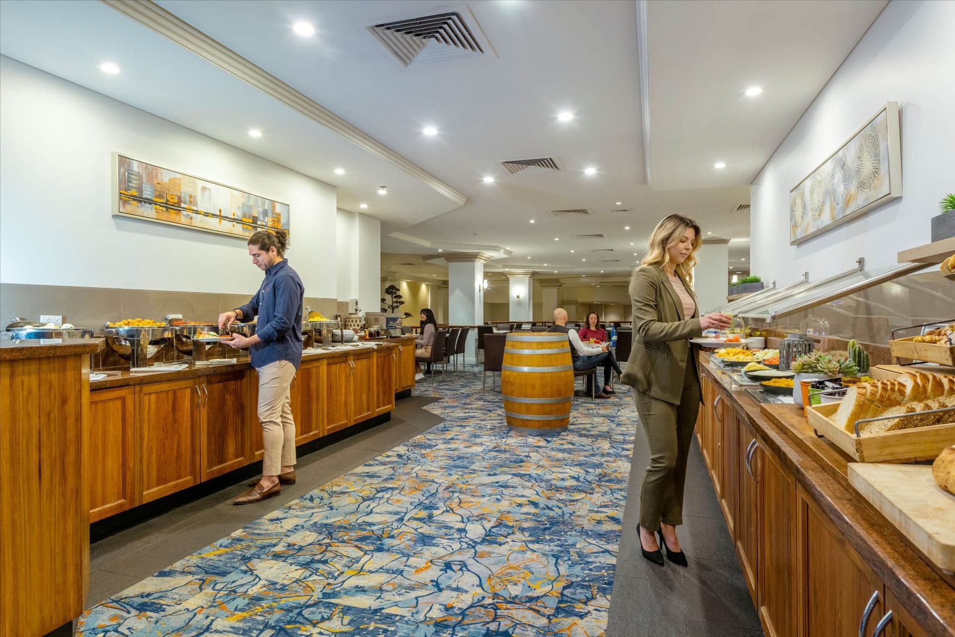 Two women in a buffet restaurant with food, wooden barrels, and modern decor at Hotel Grand Chancellor Adelaide