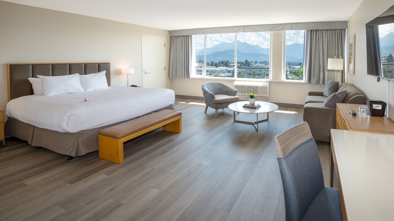 Hotel room with large bed, sofa, table, and window with mountain view.