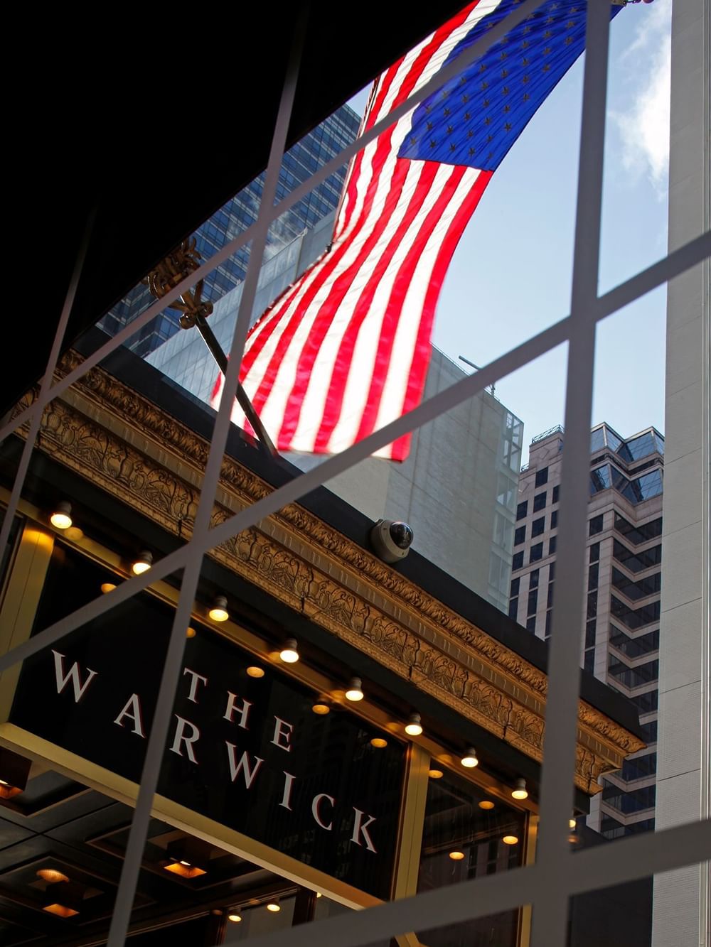 United States flag by city buildings under a blue sky, seen through a window near Warwick San Francisco
