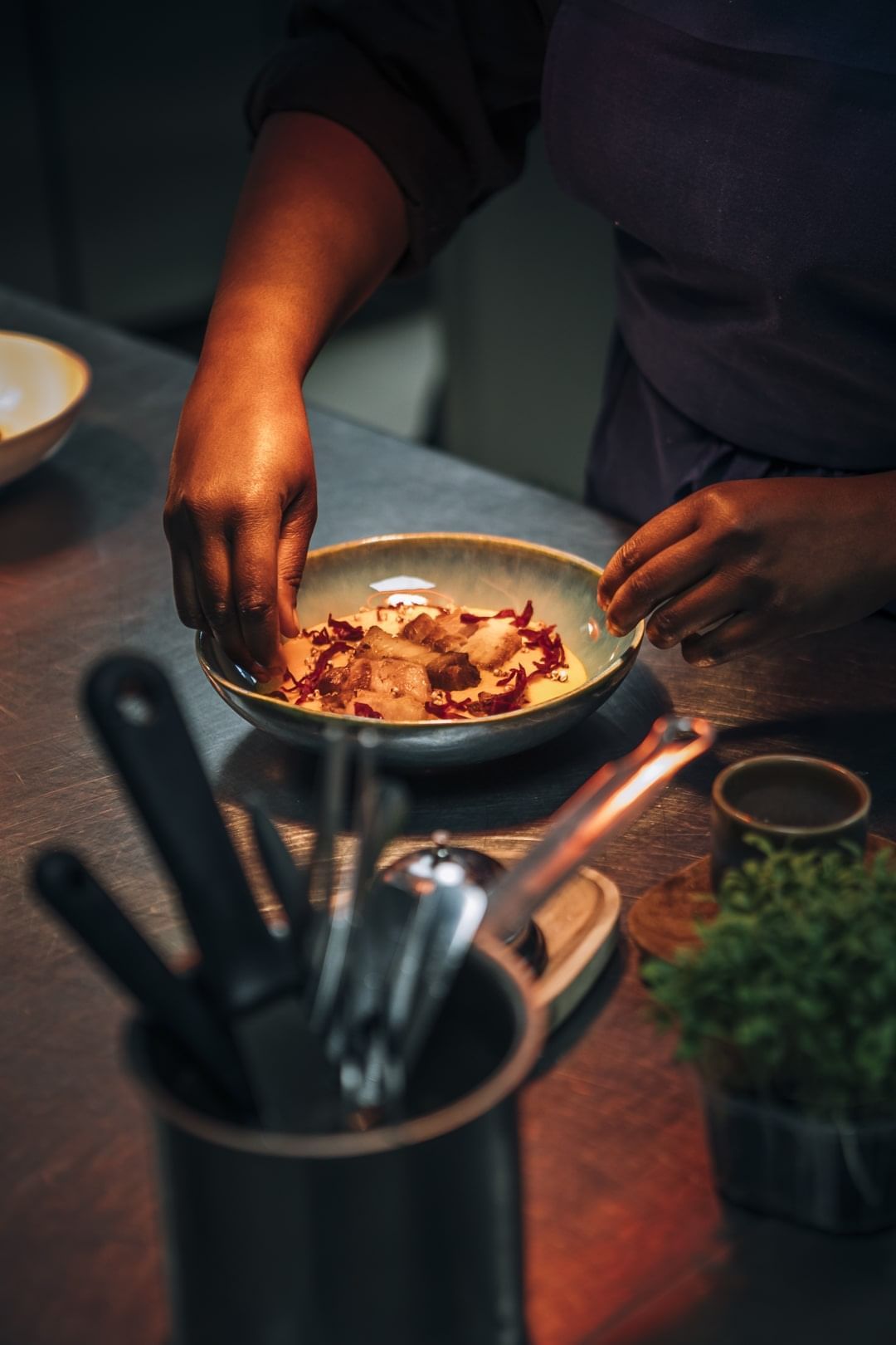 La main d'un chef garnit délicatement un plat gastronomique de pétales d'un rouge éclatant dans un bol peu profond à l'hôtel Oceania D'Anjou Angers.